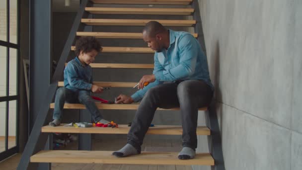 Lindo niño con papá jugando con herramientas de juguete en las escaleras — Vídeos de Stock