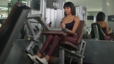 Spor salonunda bacak uzatma makinesiyle egzersiz yapan bir kadın.