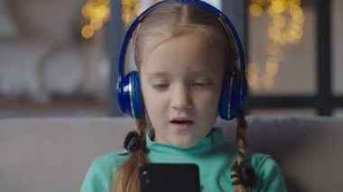 Kulaklıklı küçük kız telefonda müzik dinliyor.