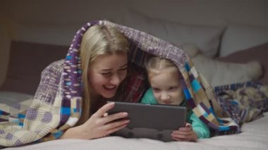 Mutlu anne ve çocuk battaniyenin altında tablet kullanıyor.