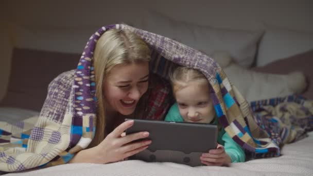 Счастливая мама и ребенок с планшетным компьютером под одеялом — стоковое видео
