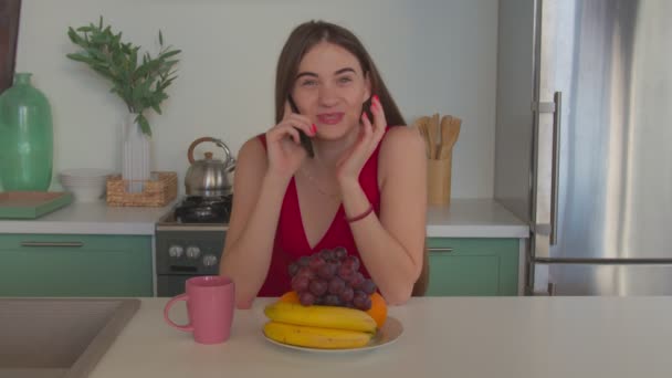 Довольно позитивная женщина говорит по телефону на кухне — стоковое видео