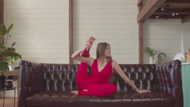 Mujer divertida flexible sentada en la pose de garza en el sofá — Vídeos de Stock