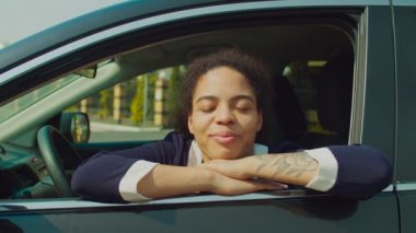 Gülümseyen siyah kadın arabanın camından dışarı bakıyor.