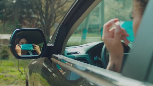 Отражение женщины в боковом зеркале автомобиля, надевающей маску — стоковое видео