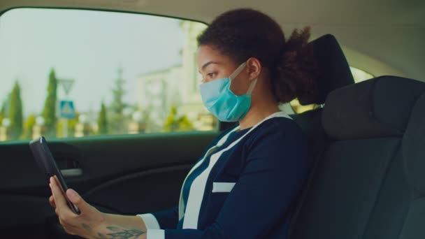 Frau mit Schutzmaske mit Tablet-PC im Auto — Stockvideo