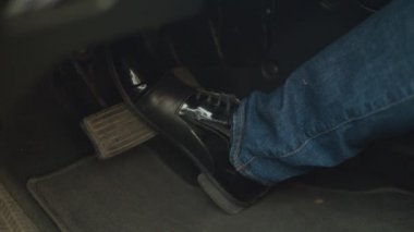 Siyah deri ayakkabılı erkek bacağı fren pedalına basıyor.