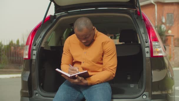 Hombre anotando horario diario sentado en el maletero del coche — Vídeo de stock