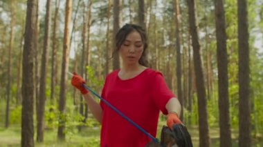 Yorgun Asyalı kadın gönüllü ormanda çöp temizliyor.