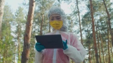 Koruyucu kıyafetli kadın bilim adamı tablet bilgisayar üzerinde çalışıyor.