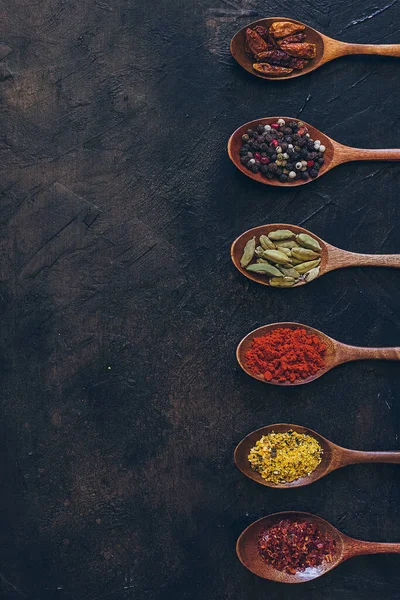 Eski siyah masada tahta kaşıklarda çeşitli baharatlar.