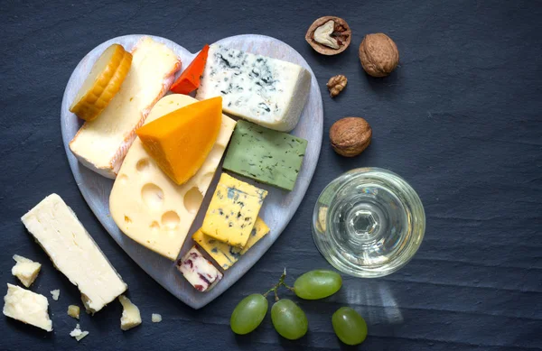 Various types of cheese on heart with glass of wine on black marble background — Stock Photo, Image