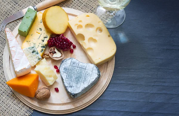 Diverse soorten kaas op een snijplank en een zwarte achtergrond — Stockfoto