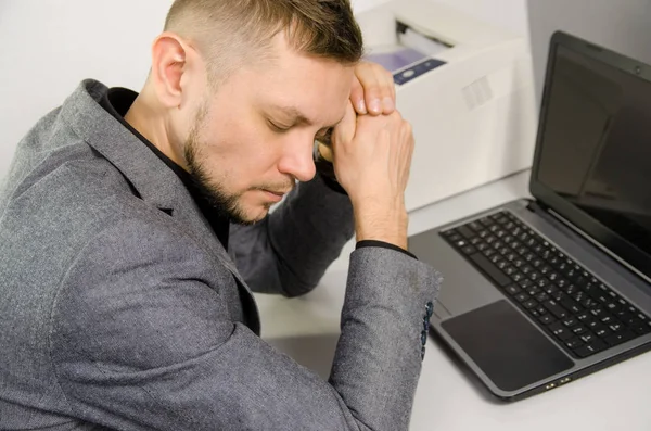 tired man with closed eyes and head leaning against hands at table