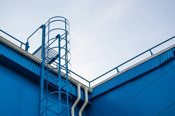 fire metal staircase on a building metal wall against a blue sky.