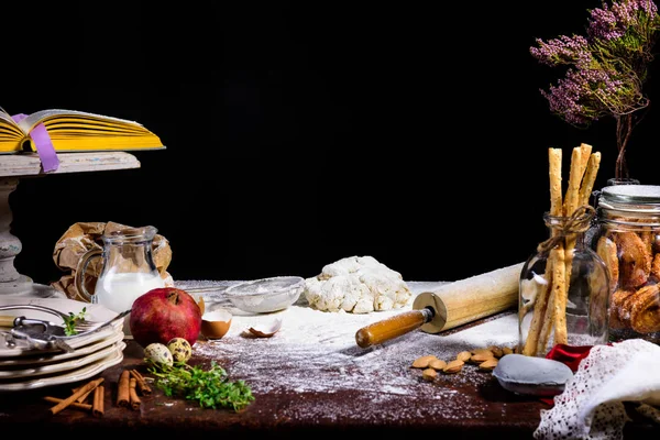 Close-up view of dough, rolling pin, dry branch and glass jug with milk on black — Stock Photo