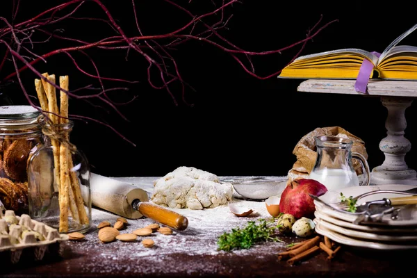 Close-up view of dough, rolling pin, dry branch and glass bottle with cookies on black — Stock Photo