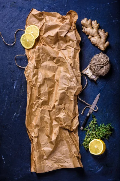 Vue du dessus du papier de cuisson froissé avec citron, gingembre, corde et couteau sur la surface bleue — Photo de stock