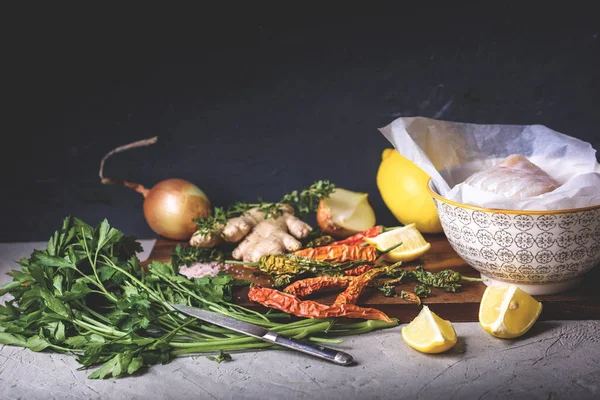 Vista close-up de peixe cru em tigela, salsa, pimentas, sal, cebola, limão e gengibre em tábua de corte de madeira — Fotografia de Stock