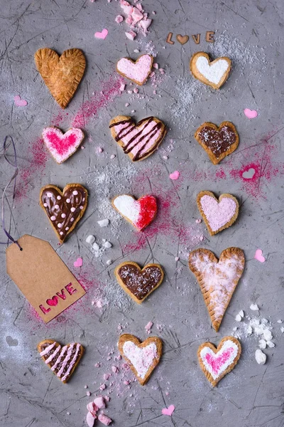 Vue de dessus des biscuits traditionnels doux en forme de coeur avec étiquette d'amour sur la surface fissurée grise — Photo de stock