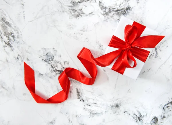 Beyaz hediye kutu kırmızı şerit yay parlak mermer arka plan — Stok fotoğraf