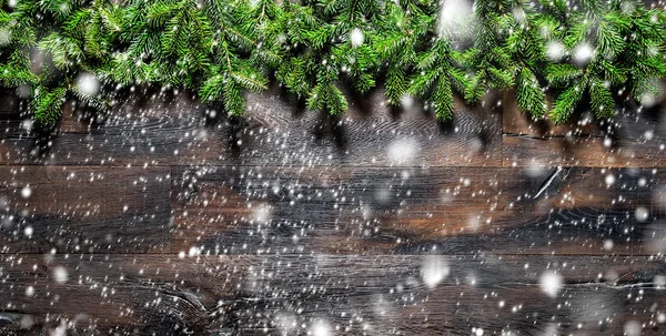 Christmas tree branches dark wooden background falling snow