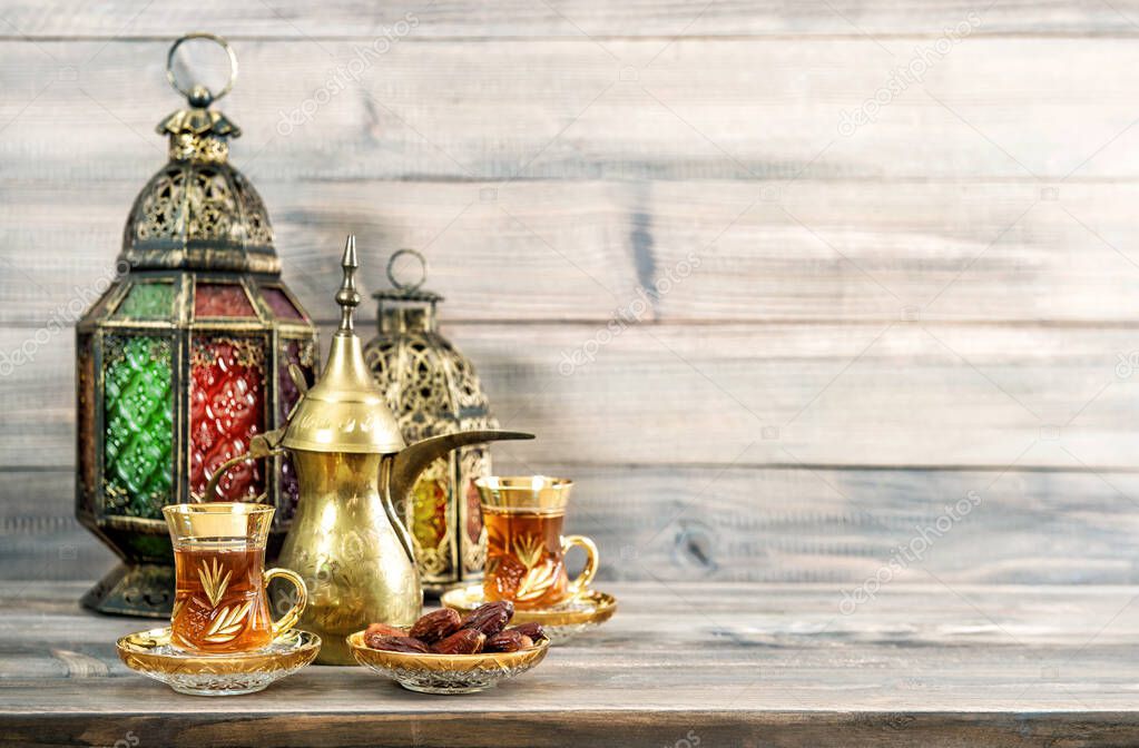 Tea glasses with dates and oriental lantern decoration on wooden background