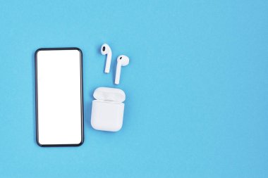 Mavi arka planda beyaz kablosuz kulaklık ve akıllı telefon..