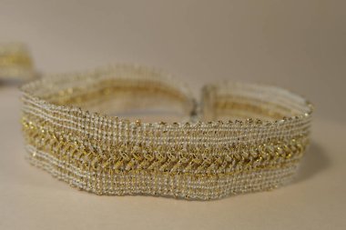 Luxury golden glow hand made decoration skin and beige color concept fashion production jewellry. Hobby lace jewellry creation fashion goods, manufacturing, handmade advertising. Vintage golden lace bracelet closeup lay on beige background.