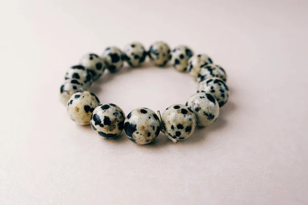 Handmade gem stone dalmatian jasper bracelet decoration product cream lies golden background. Fashion accessory bead stringing hand decoration. 