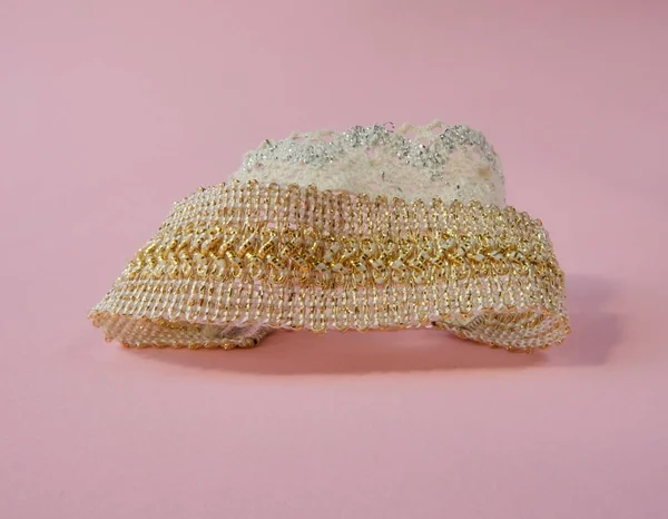 Hand made golden and silver lace pattern in hand decoration shades pink background. Hobby lace jewellry creation fashion goods, manufacturing, handiwork, weaving.