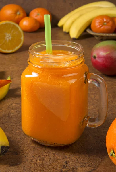 Mango orange banana and tangerine smoothie with ingredients on a brown background. Selected focus.