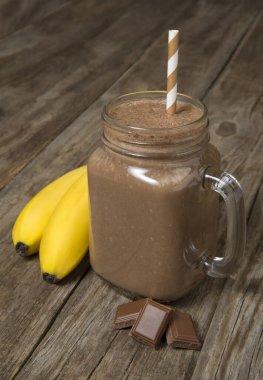 Kırsal ahşap bir masada malzemelerle dolu cam bir kavanozda muzlu çikolatalı smoothie. Seçili odak.