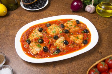 Kahverengi bir masada domatesli ve zeytinli tavada kurutulmuş balık. Seçili odak.