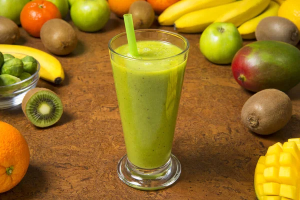 Green smoothie banana kiwi mango orange and apple in glass jar with fresh ingredients on a brown table. Selected focus.