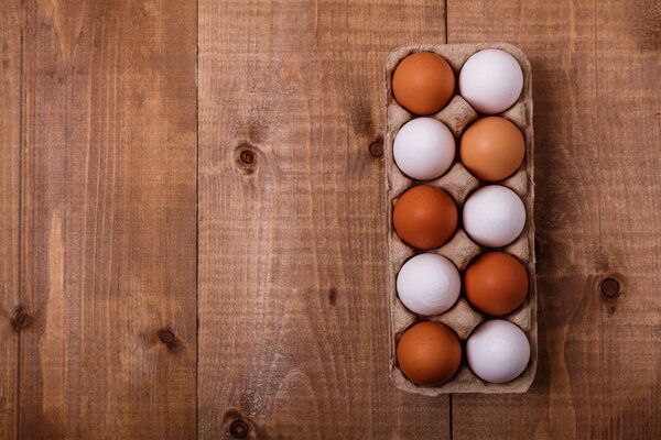 Eggs in pack on wooden table. Top view, text space