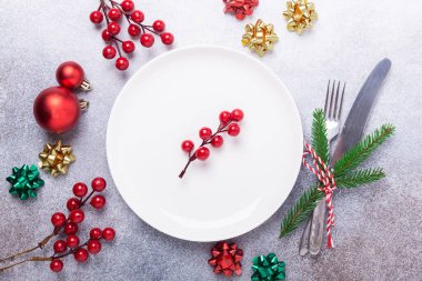 Boş beyaz tabakla Noel sofrası, taş zeminde şenlikli çatal bıçak takımı.
