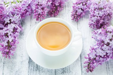 Ahşap arka planda bir fincan bitki çayı ve leylak. Güneş ışığı ışınları