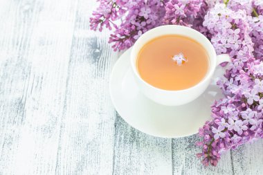 Ahşap arka planda bir fincan bitki çayı ve leylak. Güneş ışığı ışınları