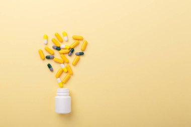 Sarı arka plandaki plastik şişeden çok renkli tabletler ve haplar çeşitli tabletler ve haplar.