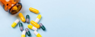 Mavi arkaplandaki cam şişeden çok renkli tabletler ve hap kapsülleri