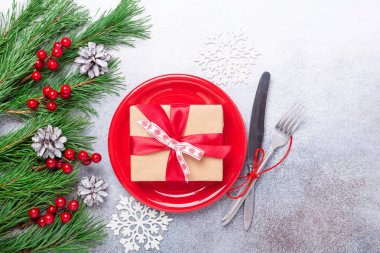 Boş kırmızı tabakla Noel sofrası, taştan arka planda şenlikli çatal bıçak takımı.