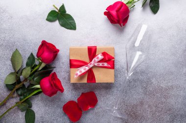 Kırmızı gül buketi, hediye kutusu, arka planda şampanya bardakları Sevgililer Günü tebrik kartı