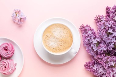 Leylak, bir fincan kahve, ev yapımı marşmelov, pembe arka planda not defteri. Durgun hayat. Bahar romantik havası. Üst görünüm