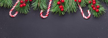 Noel arkaplanı ağaç dalları, baston şekerler ve siyah ahşap arka planda çobanpüskülü. Kar yağışı çizim efekti.