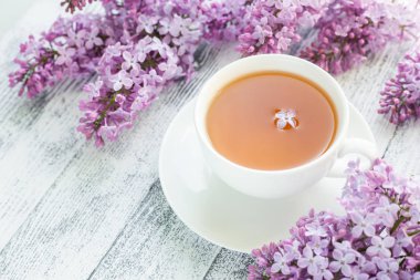 Ahşap arka planda bir fincan bitki çayı ve leylak. Güneş ışığı ışınları