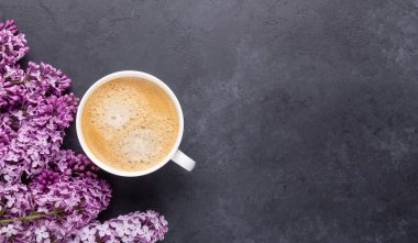 Kahveli beyaz bardak ve siyah taştan arka planda leylak çiçekleri. Uzayı kopyala Üst görünüm