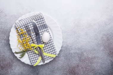 Paskalya sofrası. Beyaz tabak, mimoza çiçekleri ve taş zeminde çatal bıçak takımı. Üst görünüm