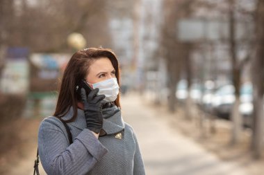 Dışarıda koruyucu tıbbi maske takan bir kadın, yakın çekim. Elinde telefon olan bir kadın. Kişisel bakım kavramını - Görüntü