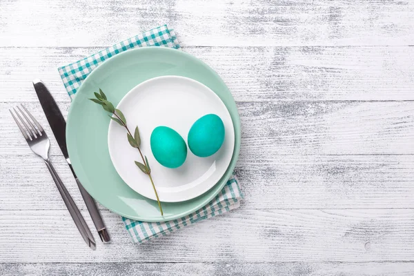 Paskalya yumurtaları ve ahşap arka planda çatal bıçak takımı olan beyaz ve yeşil nane tabağı. Paskalya kompozisyonu. Uzayı kopyala Üst Görünüm - Resim